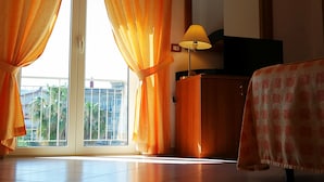 Habitación de hotel con un amplio ventanal corredero, un armario de madera, una lámpara y una toalla de cuadros sobre una silla.