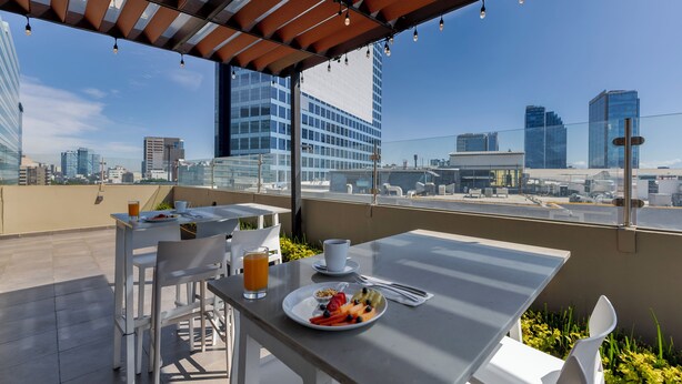 Terraza en la azotea con una mesa dispuesta para el desayuno, que incluye un plato de fruta y un vaso de zumo de naranja.