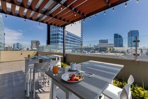 Terraza en la azotea con una mesa dispuesta para el desayuno, que incluye un plato de fruta y un vaso de zumo de naranja.