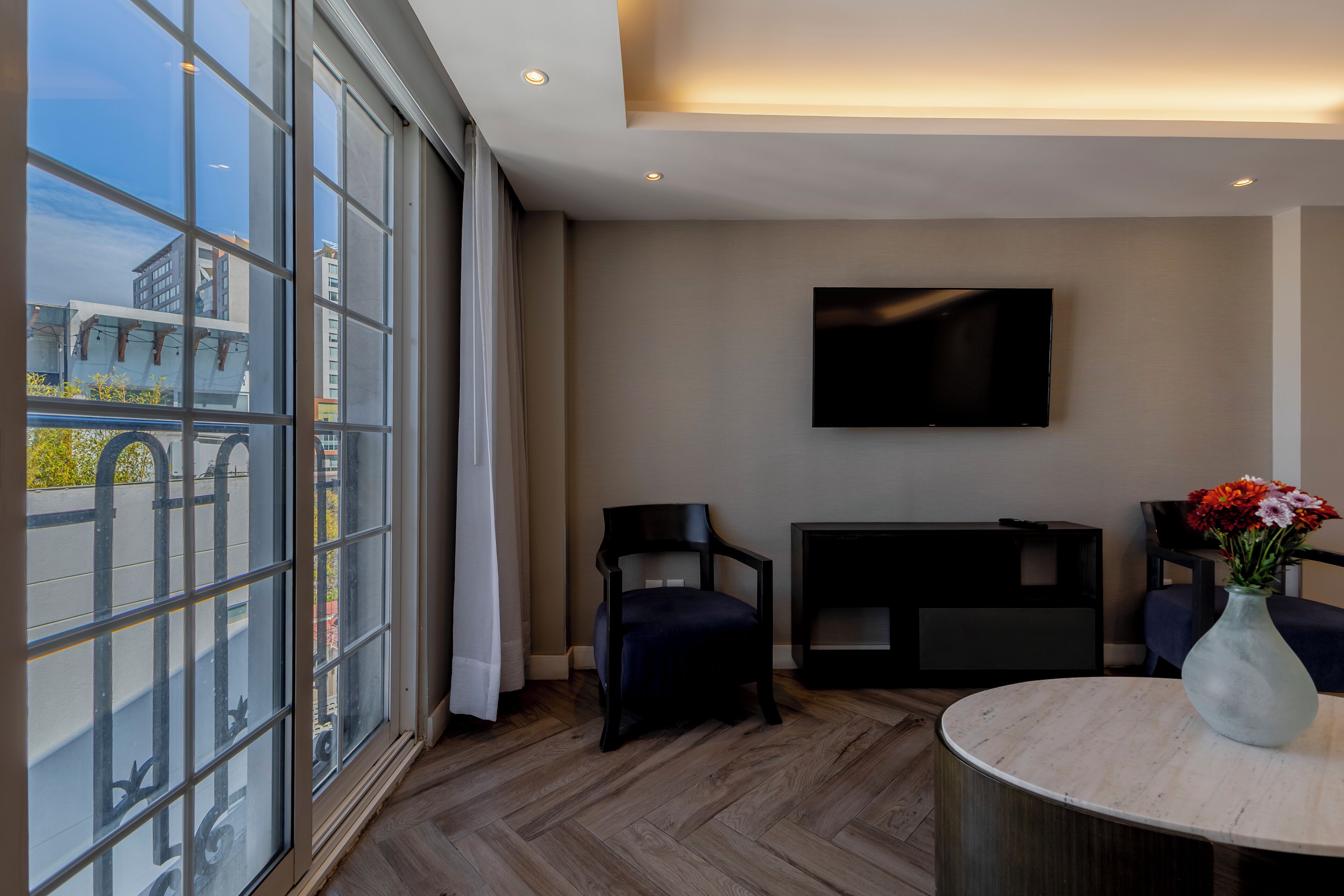 A modern living room with a large window, a flat-screen TV, and a round table with a vase.