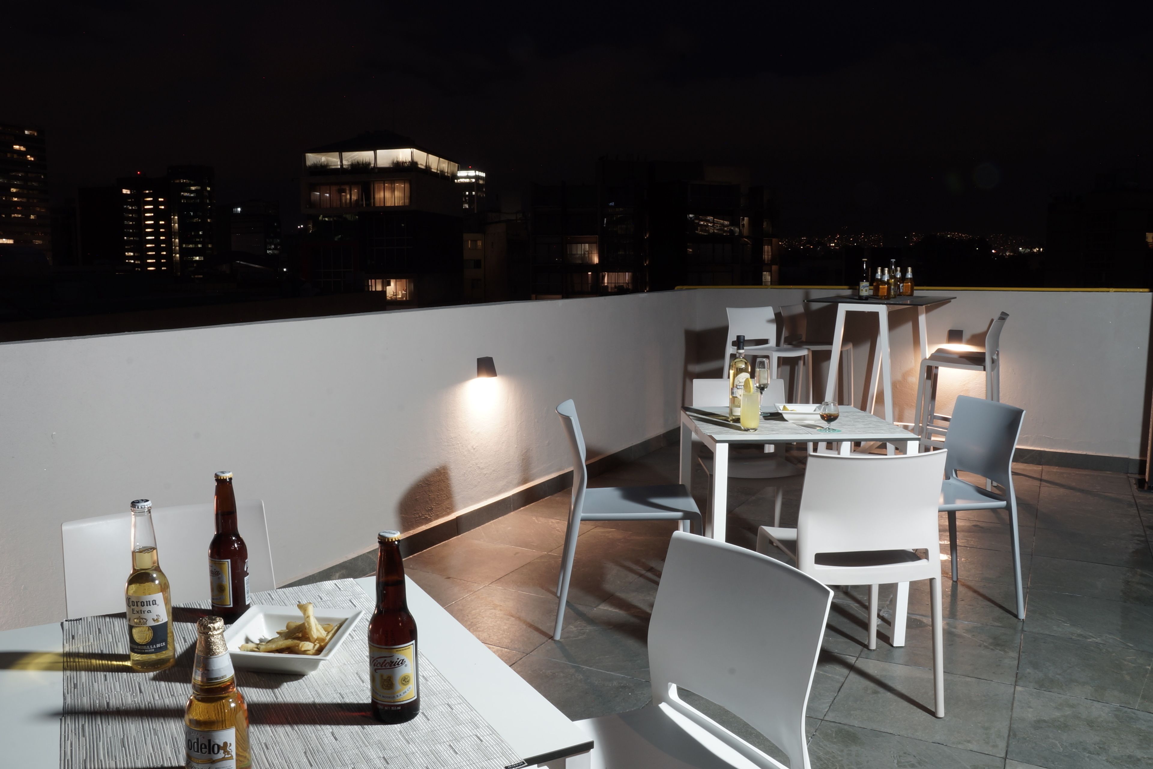 Ein Dachterrassen-Essbereich mit Tischen, Stühlen, Bierflaschen und einem Teller Essen.