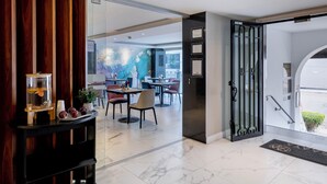 Un vestíbulo de hotel moderno con suelo de mármol, una recepción y un área de comedor al fondo.