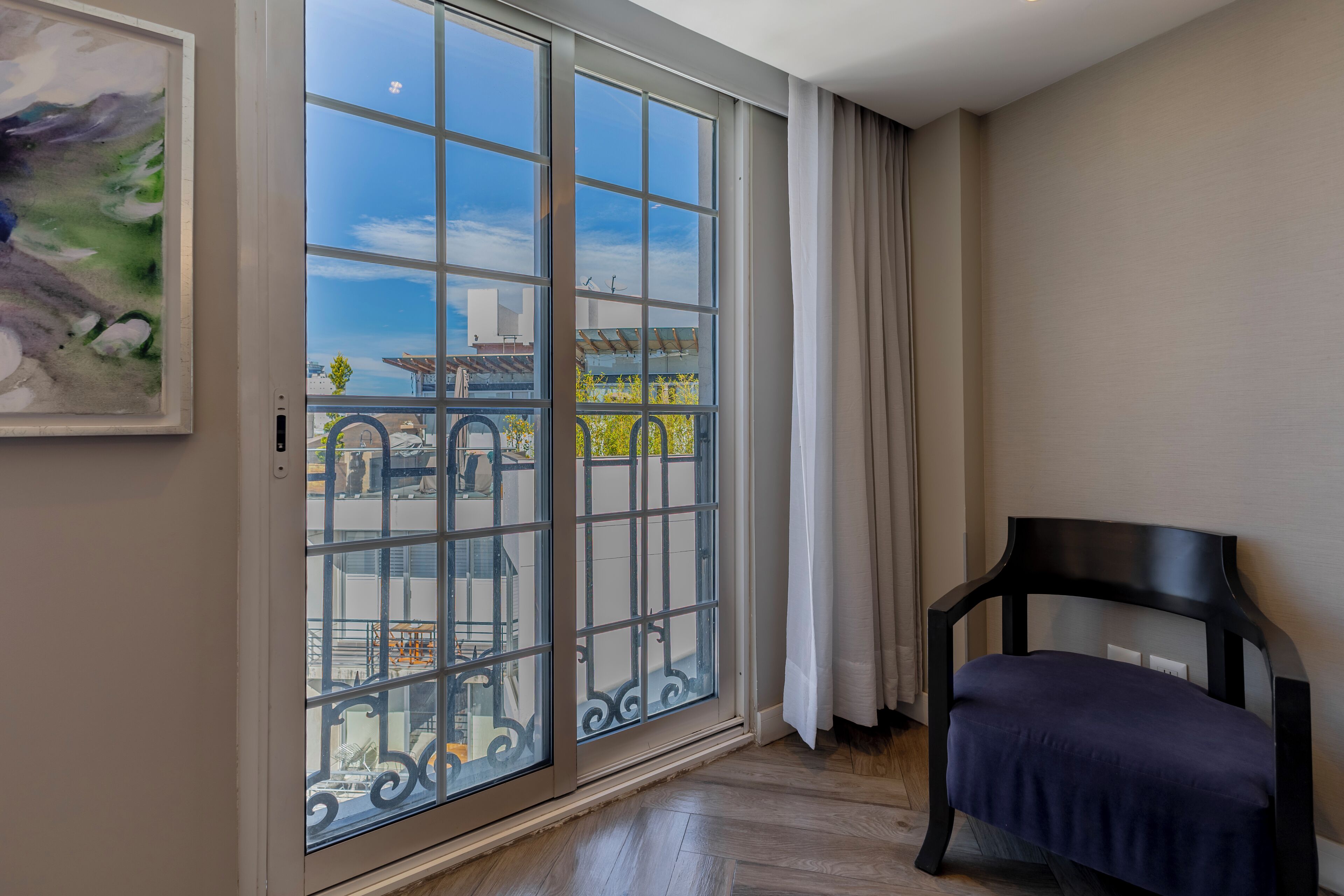 Ein Zimmer mit einer großen Schiebeglasdoor zum Balkon, einem schwarzen Stuhl und einem Bild an der Wand.