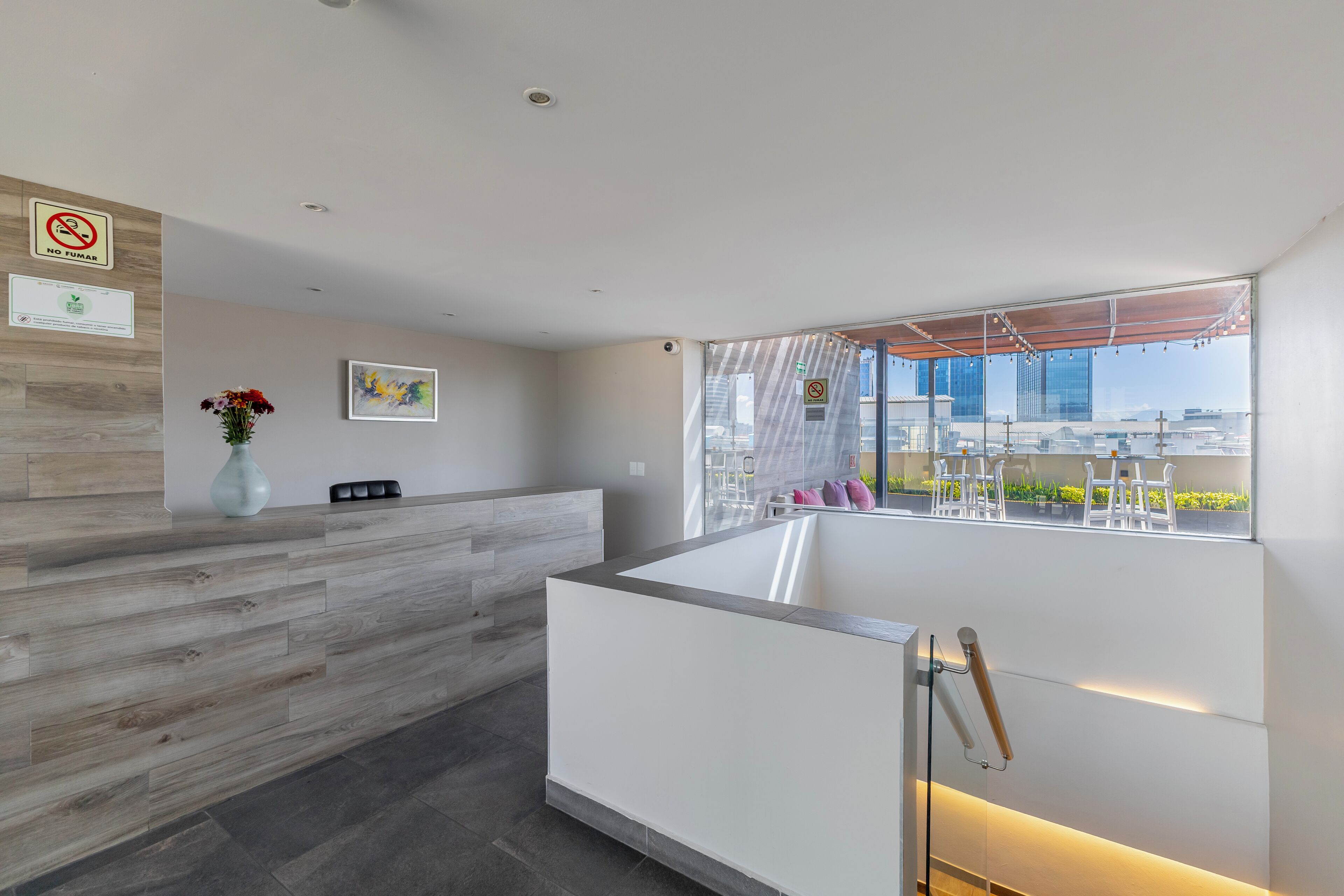 A modern reception area with a wooden reception desk, a vase of flowers, and a view of the city through large windows.