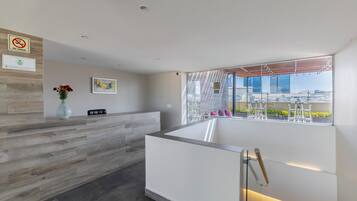 A modern reception area with a wooden reception desk, a vase of flowers, and a view of the city through large windows.
