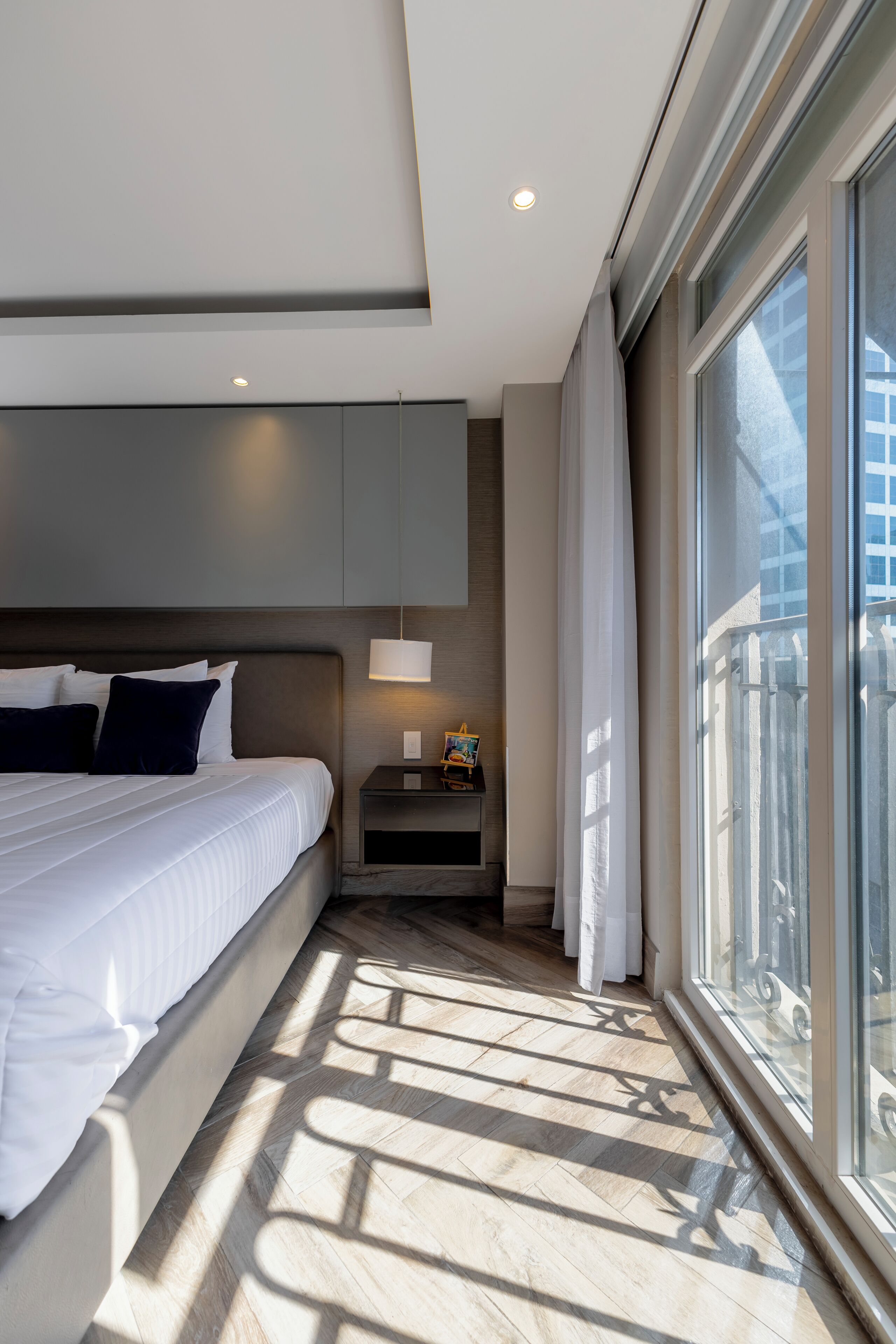 Een moderne hotelkamer met een groot bed, een nachtkastje, een lamp en uitzicht op de stad door grote ramen.