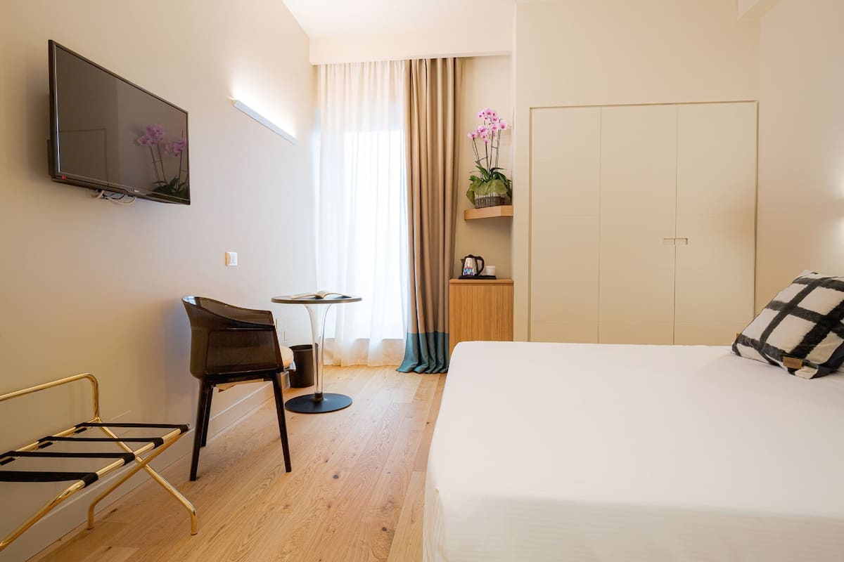 Habitación de hotel con cama, escritorio, silla, televisor, ventana con cortinas y armario.