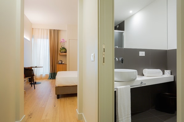 A hotel room with a bed, a desk, a chair, a bathroom with a sink, mirror, and towel rack. - Hotel Politeama (Palermo)
