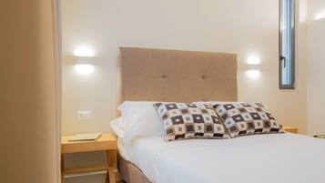 Cama bem arrumada com cabeceira, dois travesseiros e mesa de cabeceira com abajur.