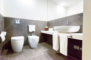 Un bagno moderno con un water, un bidet e un ampio lavabo con piano in marmo.
