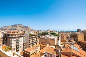 Un paisaje urbano con una montaña destacada al fondo, una combinación de edificios residenciales y comerciales, y un cielo azul despejado.