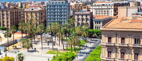 Un paisaje urbano con un edificio moderno destacado, palmeras bordeando una calle y arquitectura histórica.