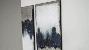 Una habitación moderna con un banco, una mesa redonda y dos grandes cuadros abstractos en la pared.
