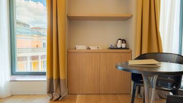 Quarto de hotel com um armário de madeira, uma mesinha com uma cadeira e uma janela com cortinas.