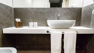 Une salle de bain moderne avec un grand lavabo blanc, des carreaux de marbre foncé et deux serviettes blanches suspendues à un porte-serviettes.