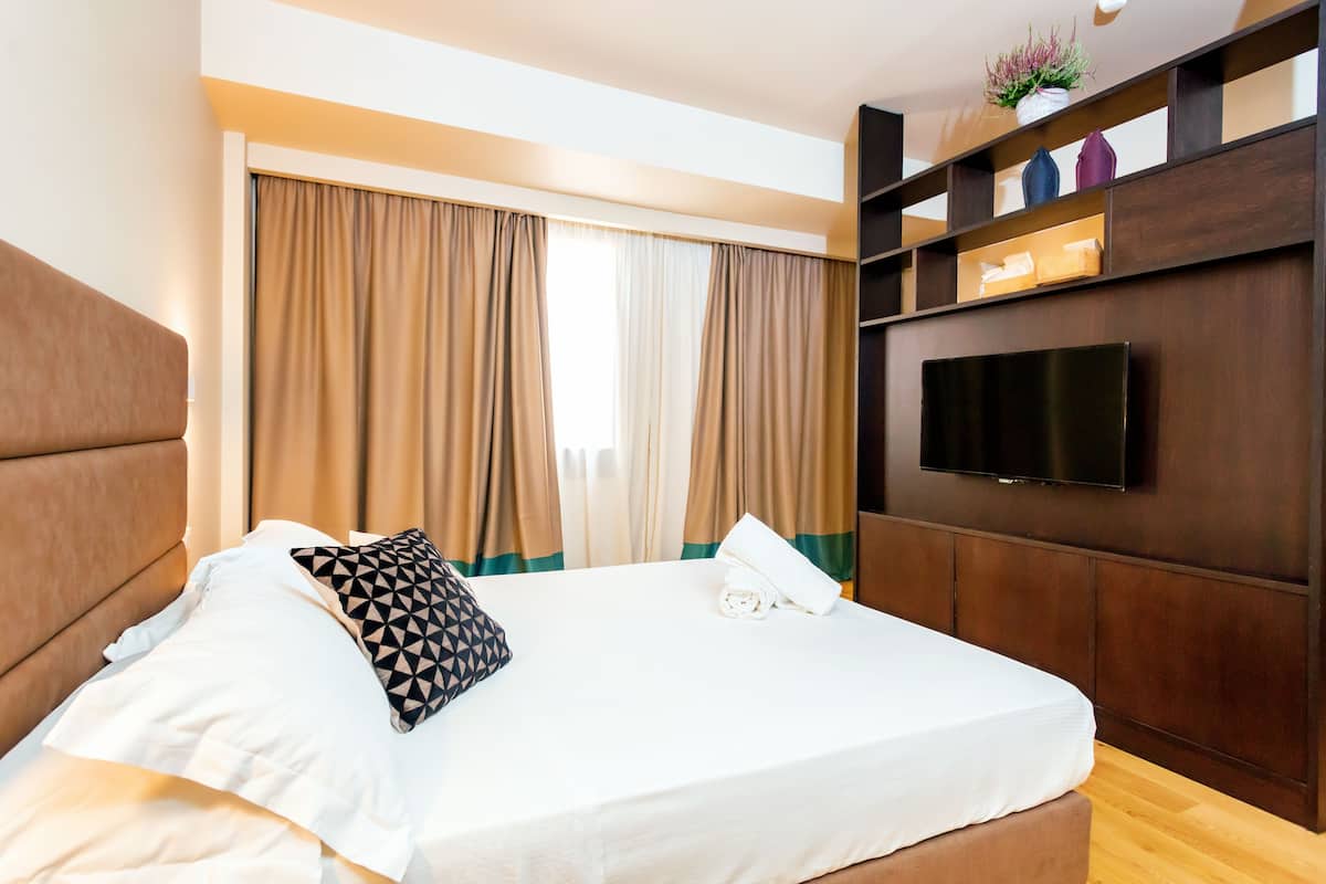 Una cama bien hecha con un cojín, una mesita de noche con un teléfono y un televisor montado en la pared.