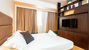 A neatly made bed with a pillow, a bedside table with a phone, and a TV mounted on the wall.