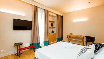 A hotel room with a bed, a TV mounted on the wall, a small desk, a bench, and a wardrobe.