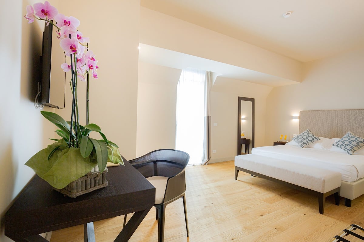 Habitación de hotel con cama, escritorio con silla, planta en maceta y espejo en la pared.
