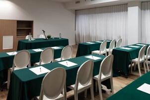 A conference room with multiple tables covered in green tablecloths, white chairs, and a microphone stand.