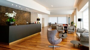 Un vestíbulo de hotel moderno con mostrador de recepción, zona de estar y grandes ventanales.