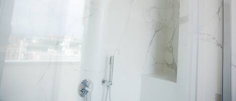 Un baño moderno con cabina de ducha de vidrio, paredes de mármol y vistas urbanas a través del ventanal.