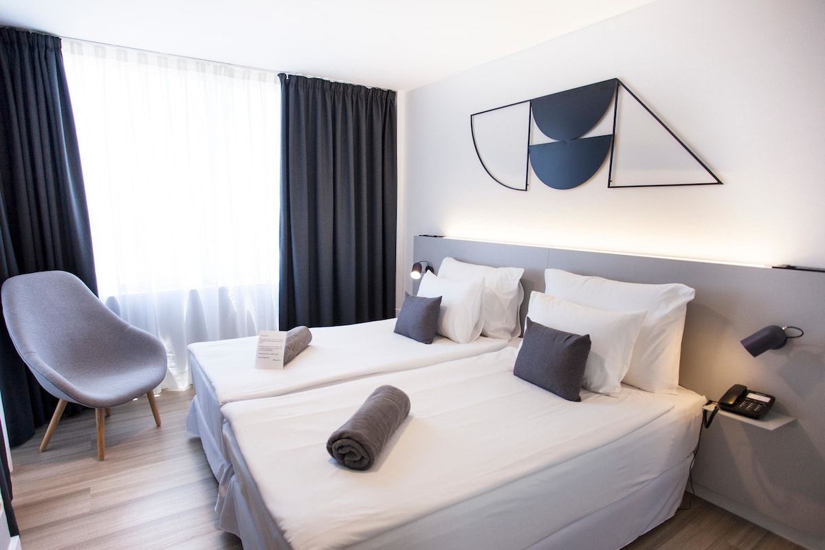 Ett hotellrum med två sängar, en stol, en telefon och en tavla på väggen.