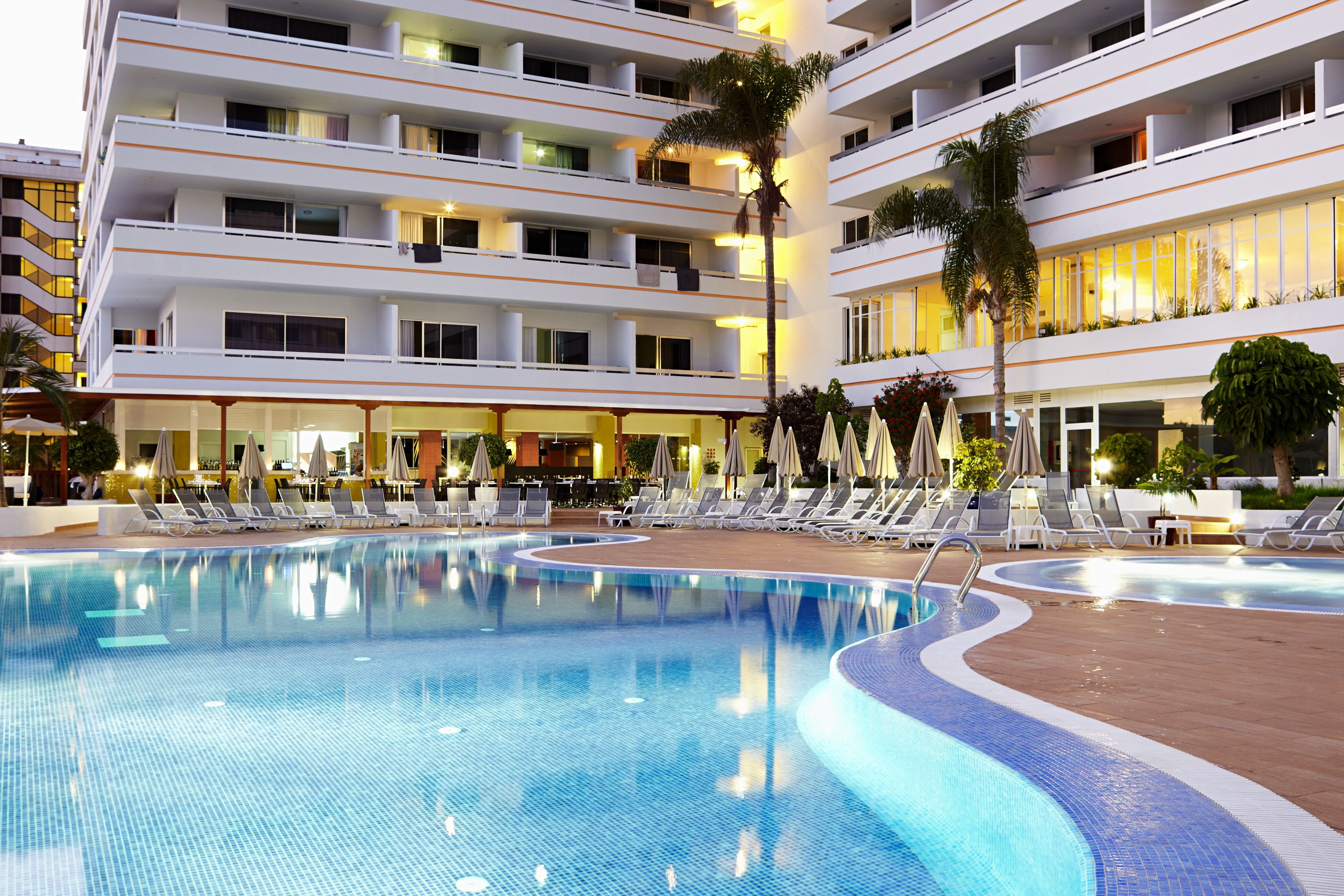 A hotel with a large swimming pool, multiple balconies, and outdoor seating areas.