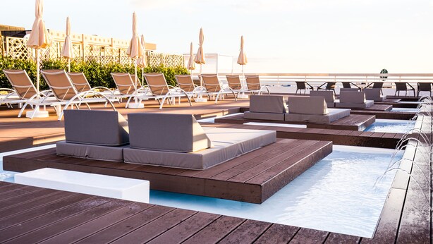 Un espace aménagé au bord de la piscine, avec des chaises longues et des transats, une terrasse en bois et une vue sur l’océan.
