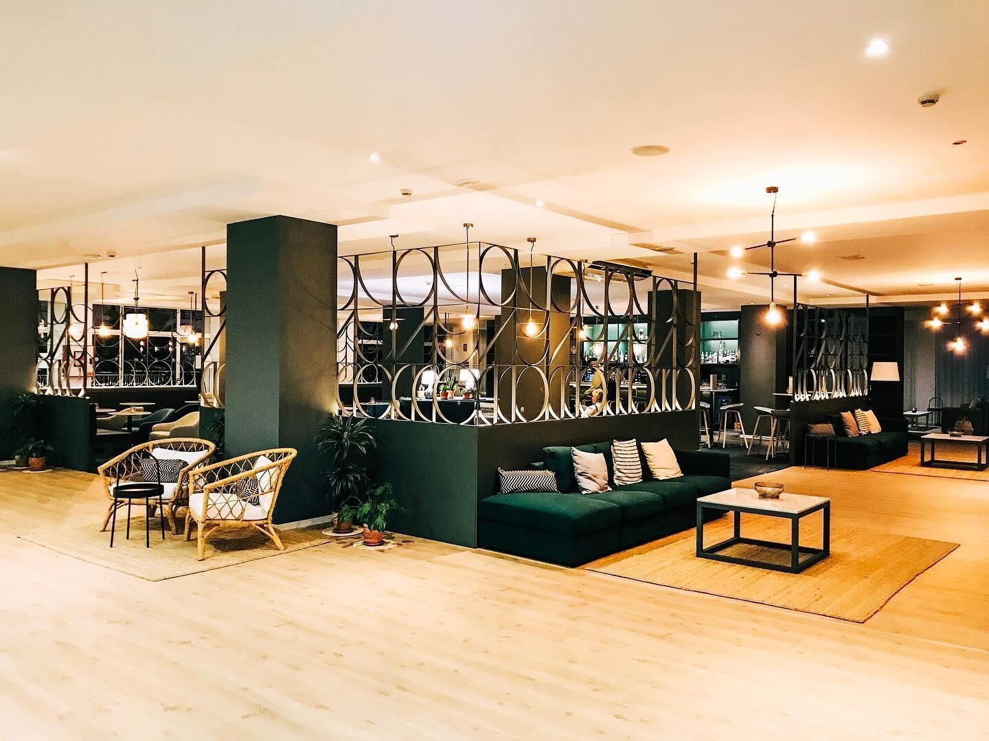 A modern interior with a green sofa, wicker chairs, a coffee table, and a decorative metal partition.