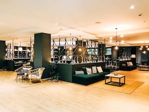 Un interno moderno con un divano verde, poltrone in vimini, un tavolino da caffè e un pannello decorativo in metallo.