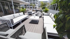 Une terrasse extérieure avec des canapés blancs, des fauteuils en osier et une table centrale.