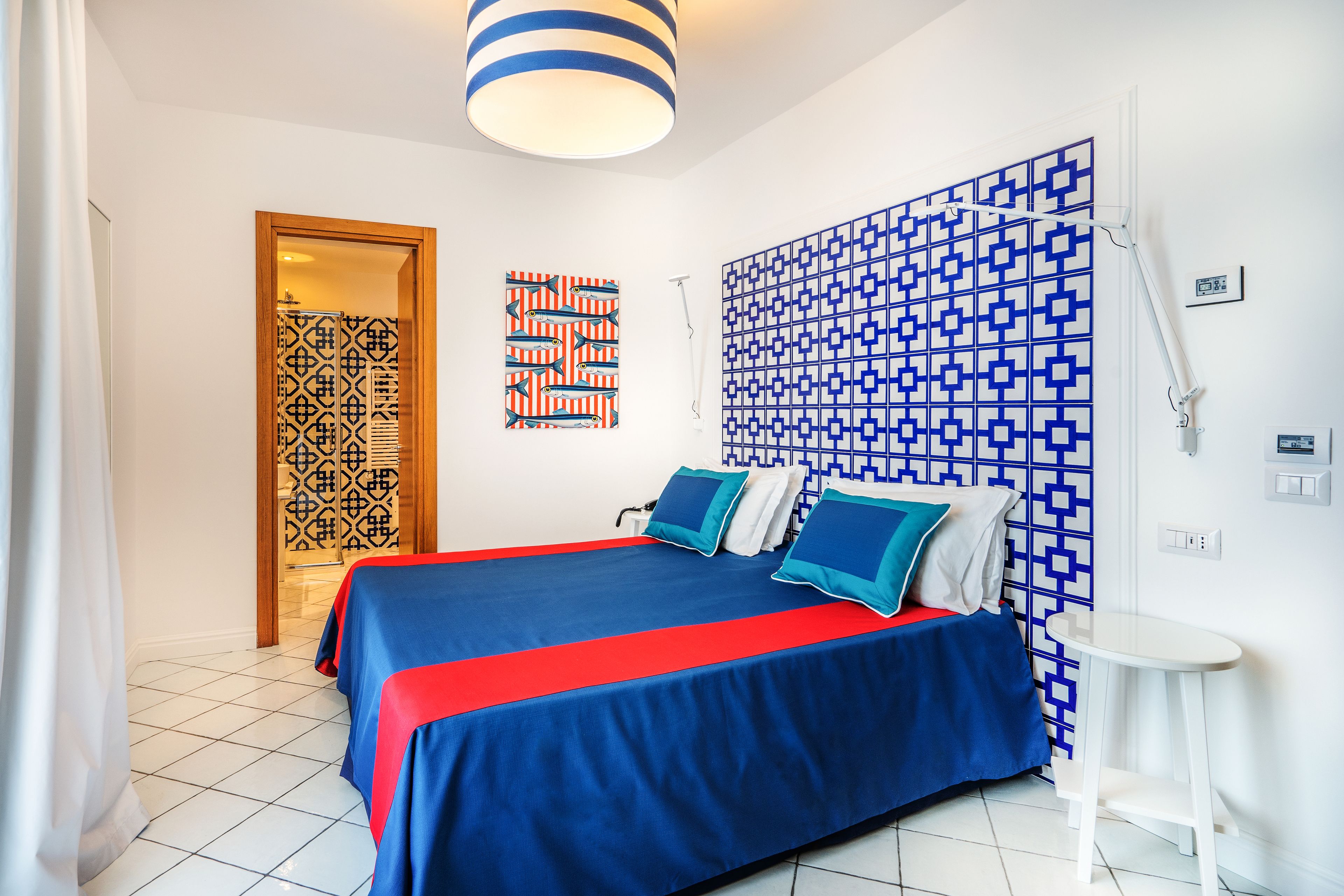 A hotel room with a bed, a nightstand, a lamp, and a patterned wall.