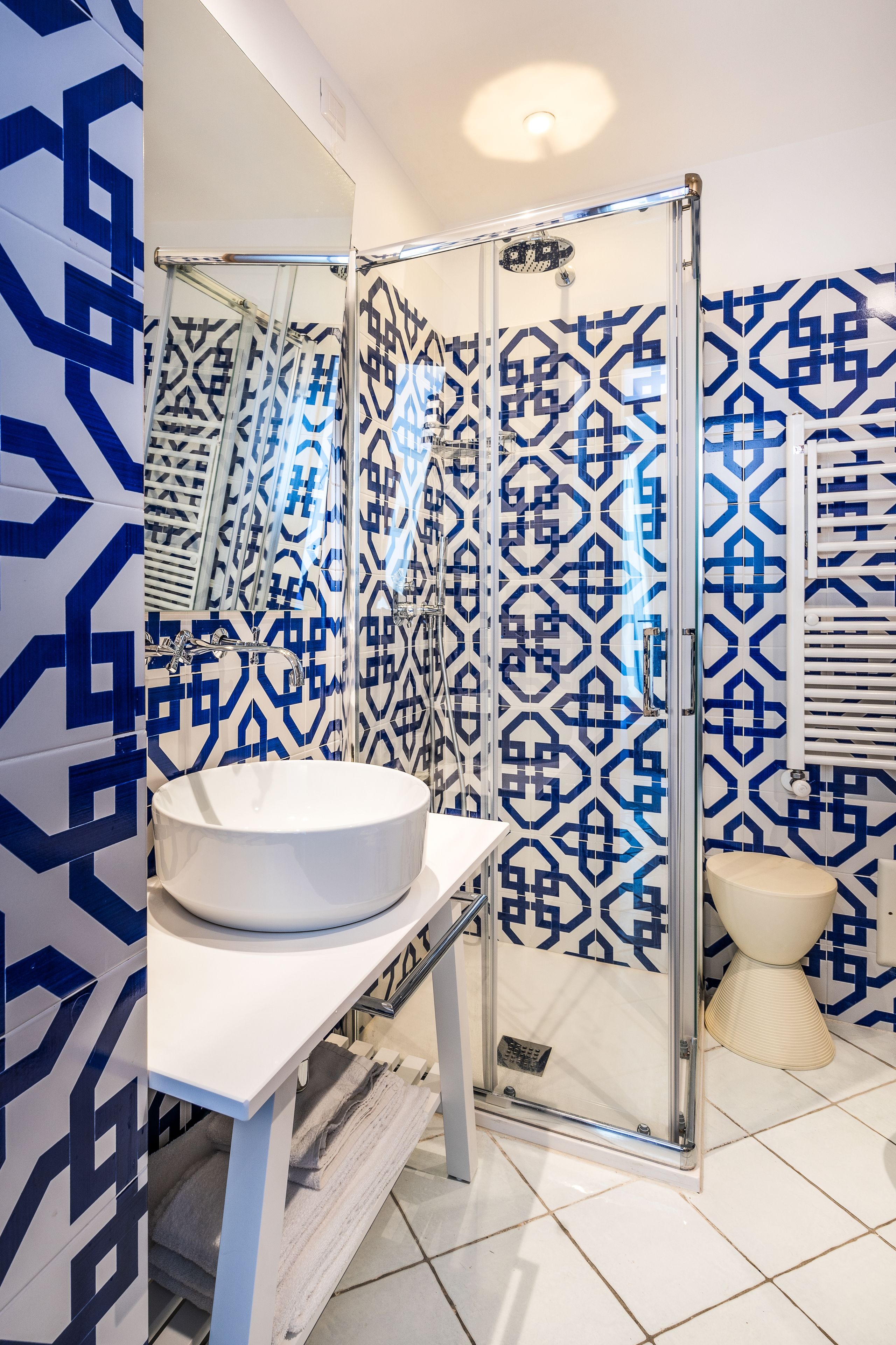 A modern bathroom with a white sink, a glass shower enclosure, and patterned tiles.