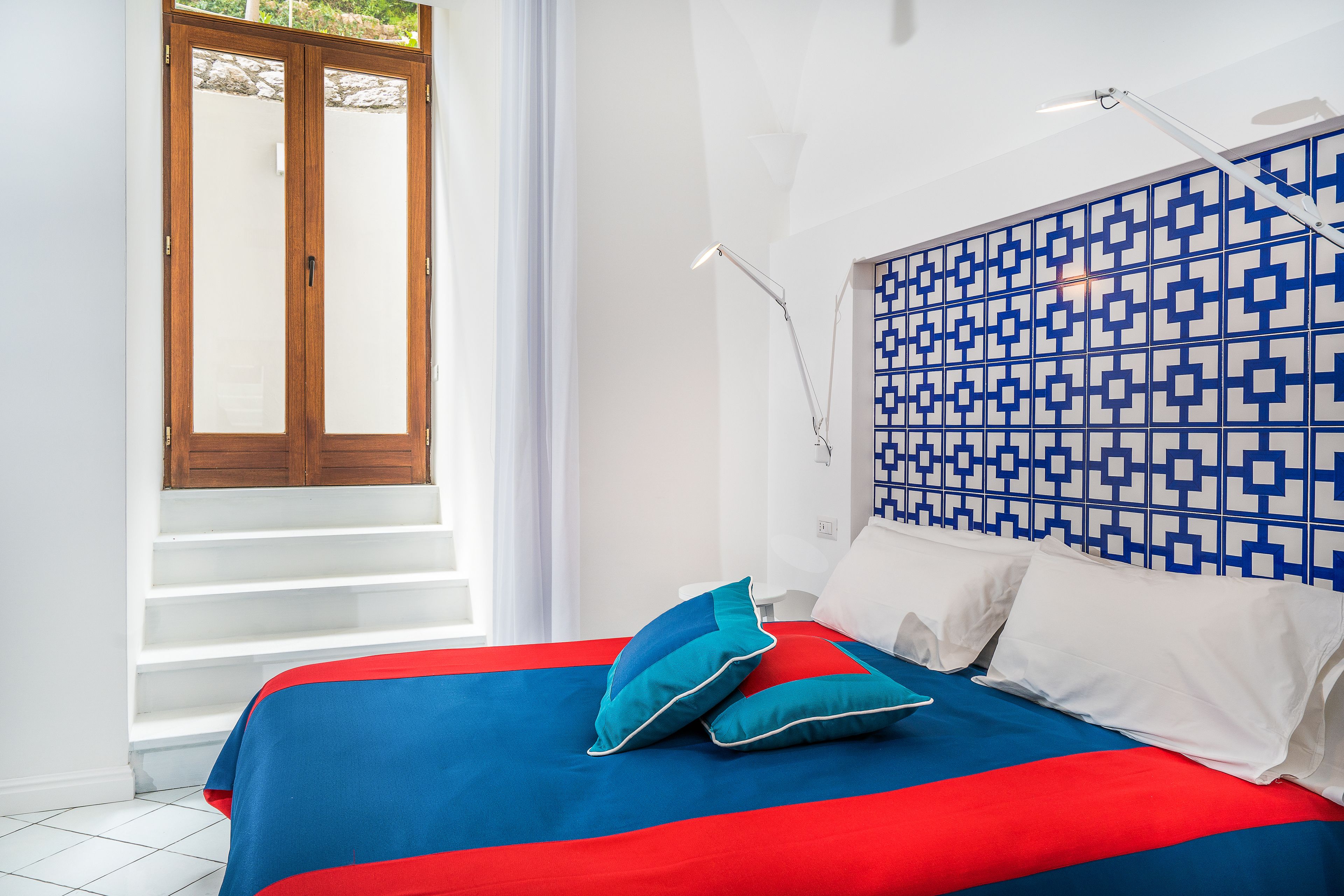 Un dormitorio con cama, cabecera estampada, ventana con cortinas y una escalera.