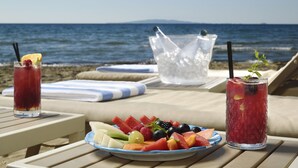 Una mesa frente al mar con una bandeja de frutas, dos bebidas y un balde de hielo.