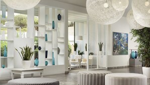 Un interior moderno con una paleta de colores blancos, que presenta un gran comedor blanco, otomanas a rayas y un estante con jarrones decorativos.
