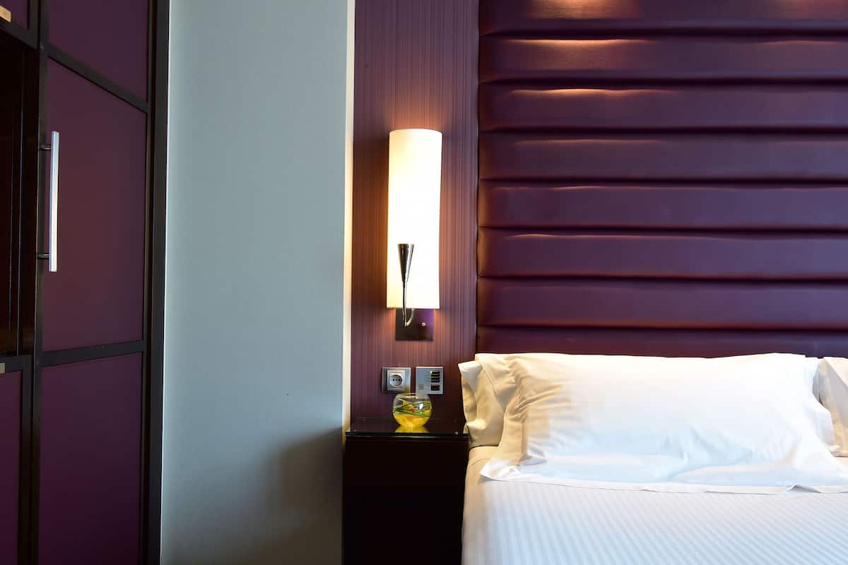 Una habitación de hotel con una cama, una mesita de noche con una lámpara y un panel en la pared.