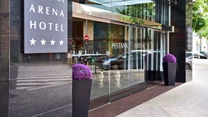 Entrada de un hotel con un letrero que dice "PESTANA ARENA HOTEL" y fachada de vidrio que refleja los alrededores.