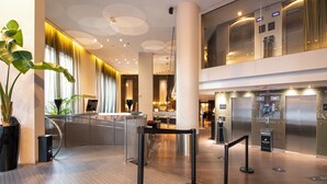 Un vestíbulo moderno de hotel con mostrador de recepción, ascensores y una escalera.