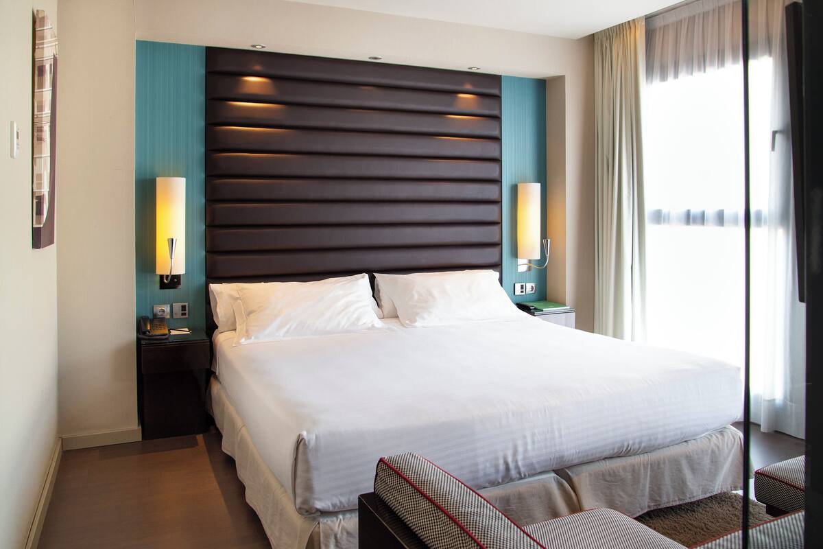 Habitación de hotel moderna con una cama grande, dos mesitas de noche y vistas a la ciudad.