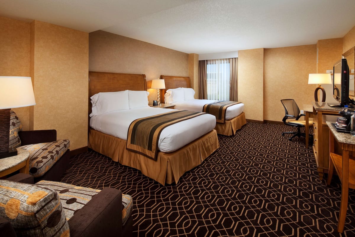 A hotel room with two beds, a desk, a chair, a lamp, and a television.