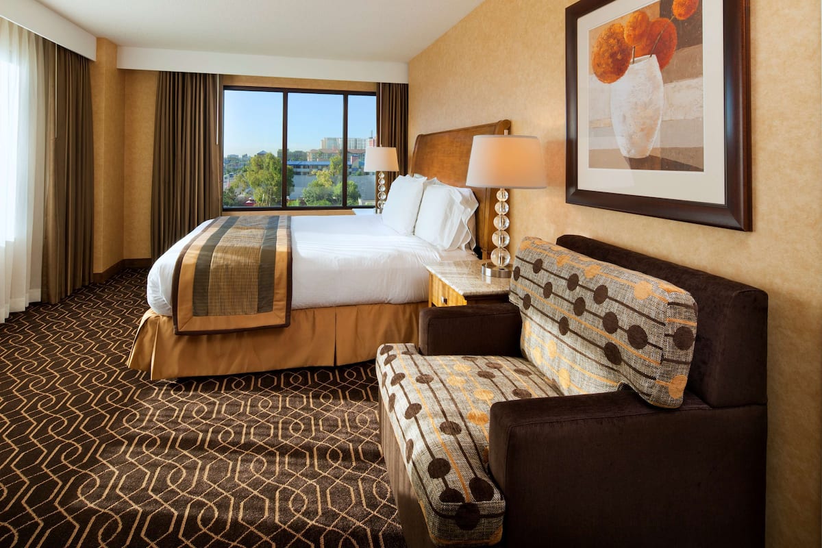 A hotel room with a large bed, a sofa, a desk, and a window with a city view.