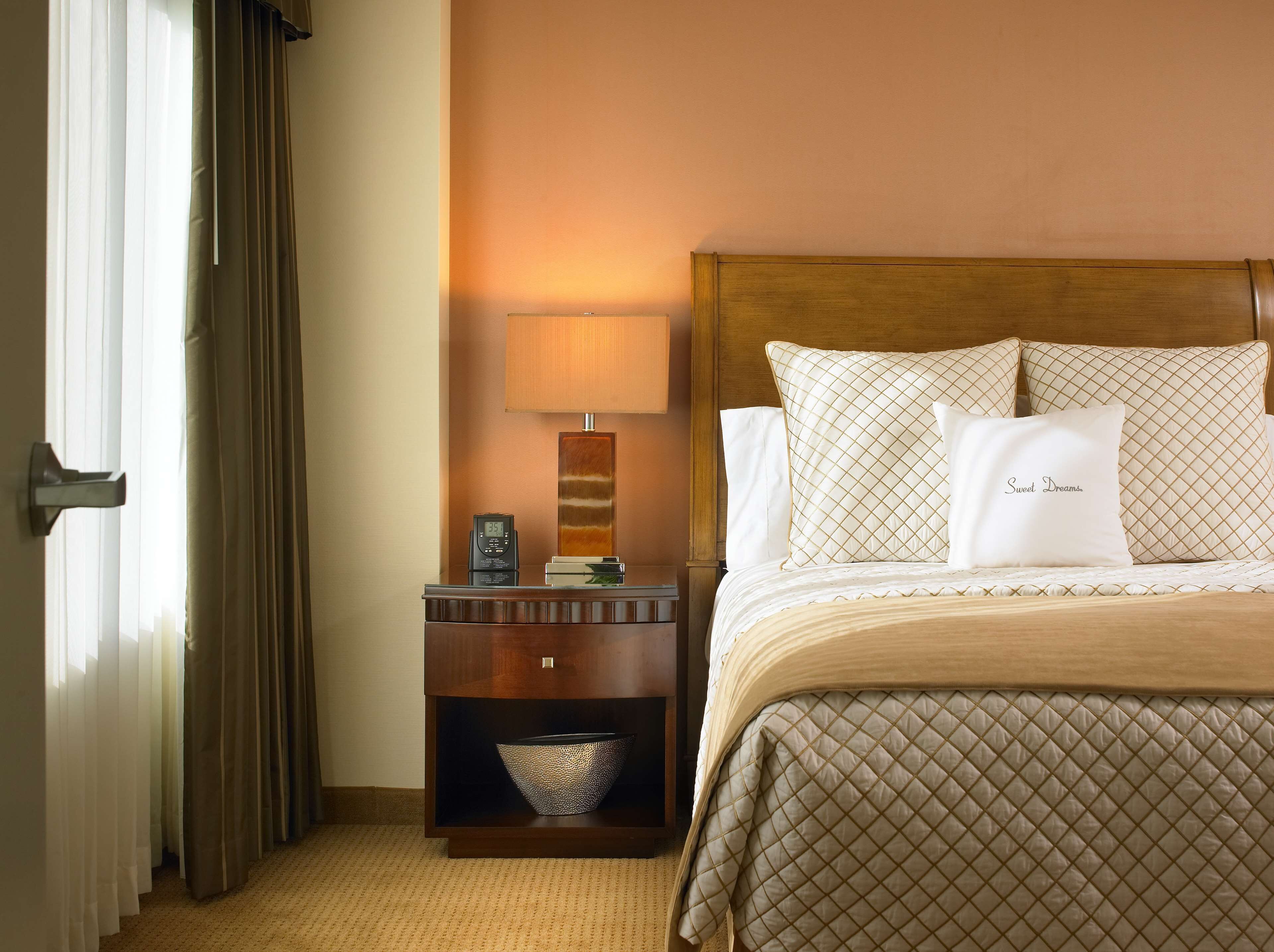 A hotel room with a bed, a nightstand, a lamp, and a window with curtains.