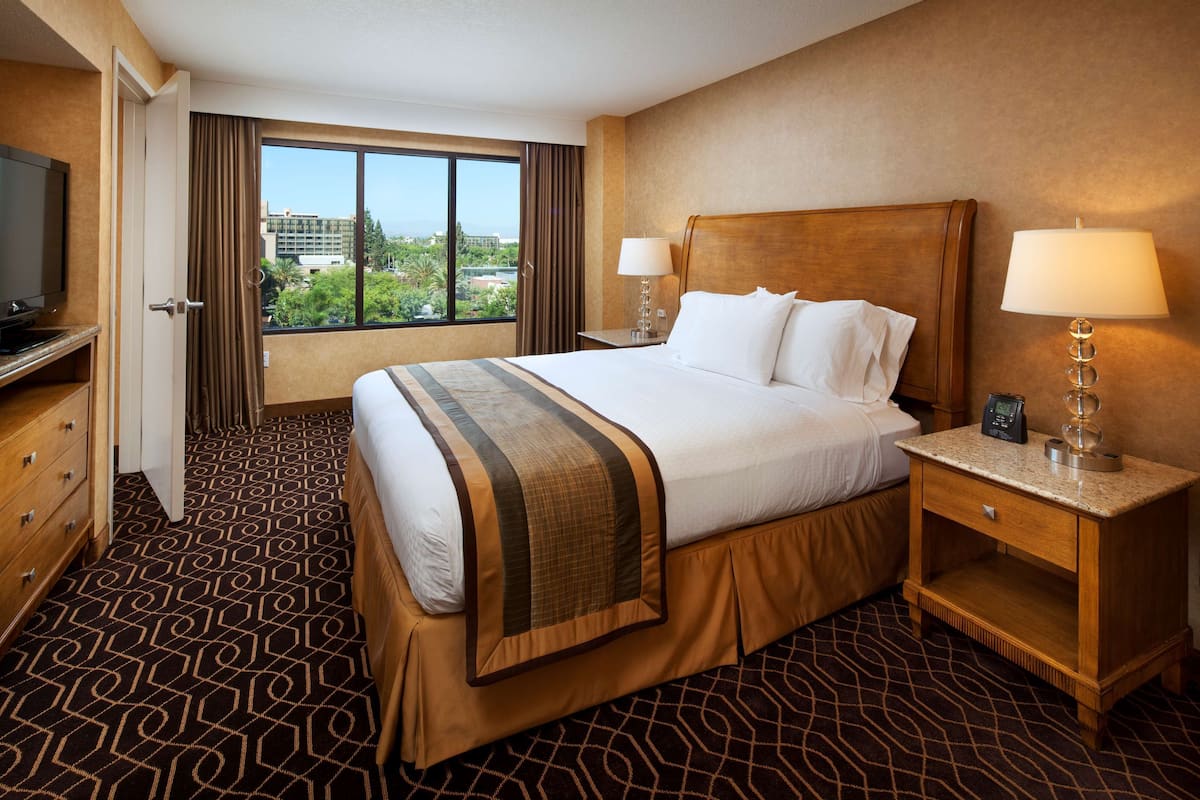 A hotel room with a large bed, a TV, a desk, and a window with a view.