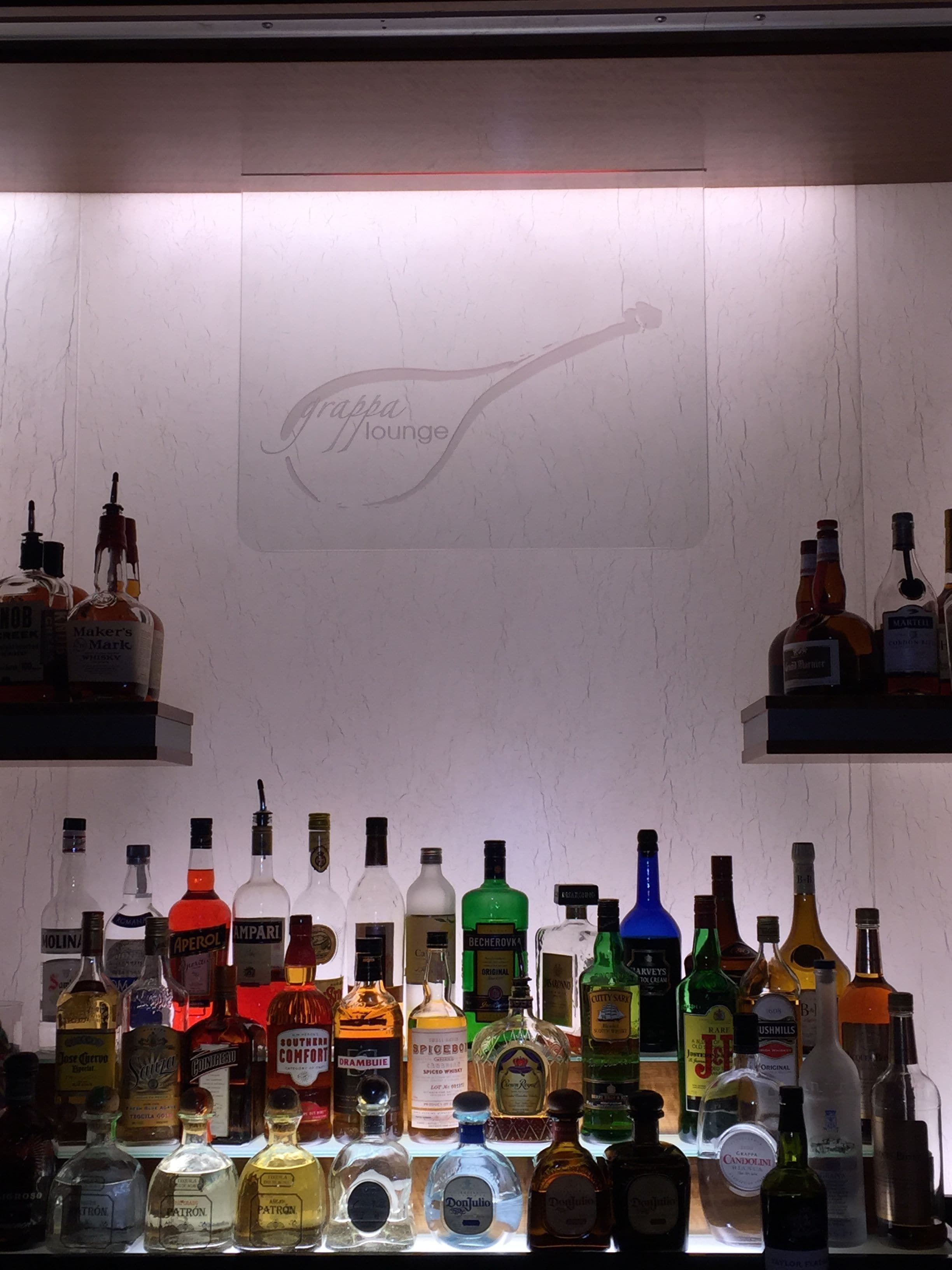 Angolo bar con diverse bottiglie di liquore e un cartello che indica 'Grappa Lounge'.