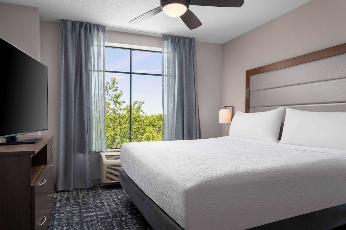Une chambre d’hôtel avec un grand lit, un téléviseur à écran plat, un ventilateur de plafond et une fenêtre avec des rideaux.