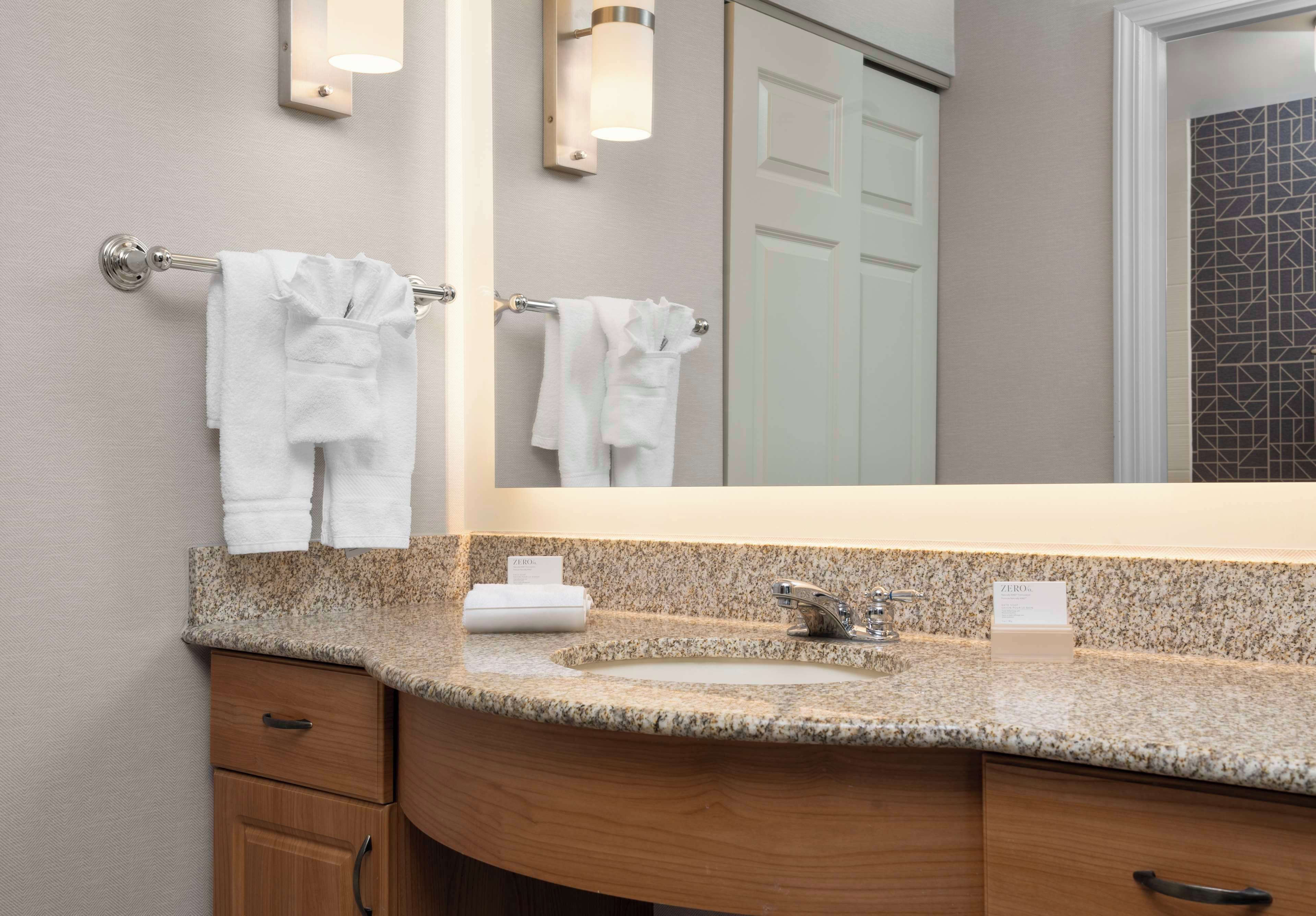 A bathroom with a granite countertop, a sink, a mirror, and two towels hanging on towel bars.