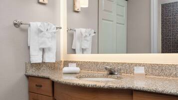 A bathroom with a granite countertop, a sink, a mirror, and two towels hanging on towel bars.