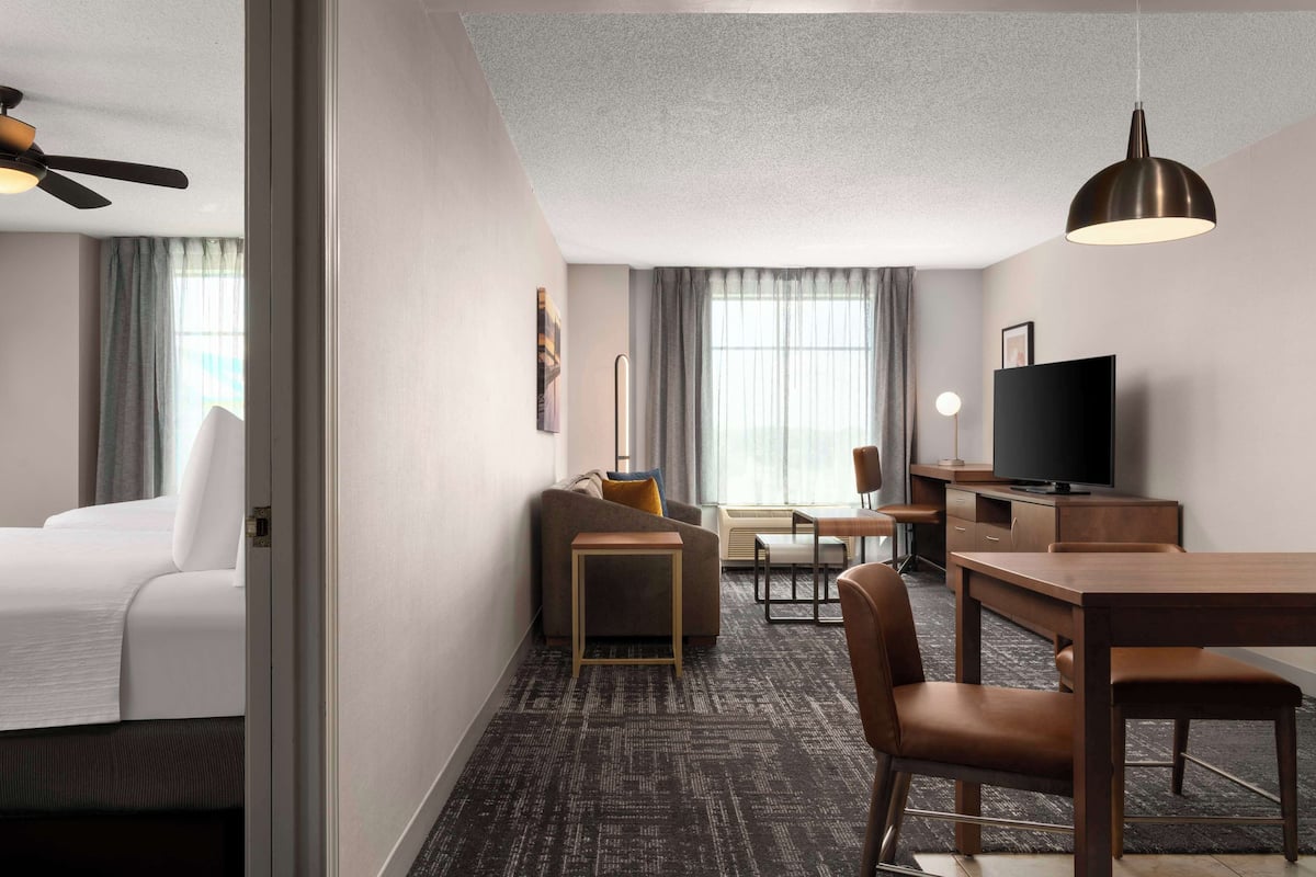 Une chambre d’hôtel comprenant un lit, un canapé, une petite table, une télévision et un coin repas avec des chaises et une table.